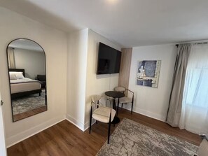 Ein Hotelzimmer mit Bett, Fernseher, einem kleinen Tisch mit Stühlen, einem Gemälde und einem Fenster mit Vorhängen.