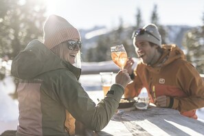 Two people sitting at a wooden table outdoors, one holding a glass. - The Peak: A Little More. A little higher. A lot more relaxed. (Kaltenbach)