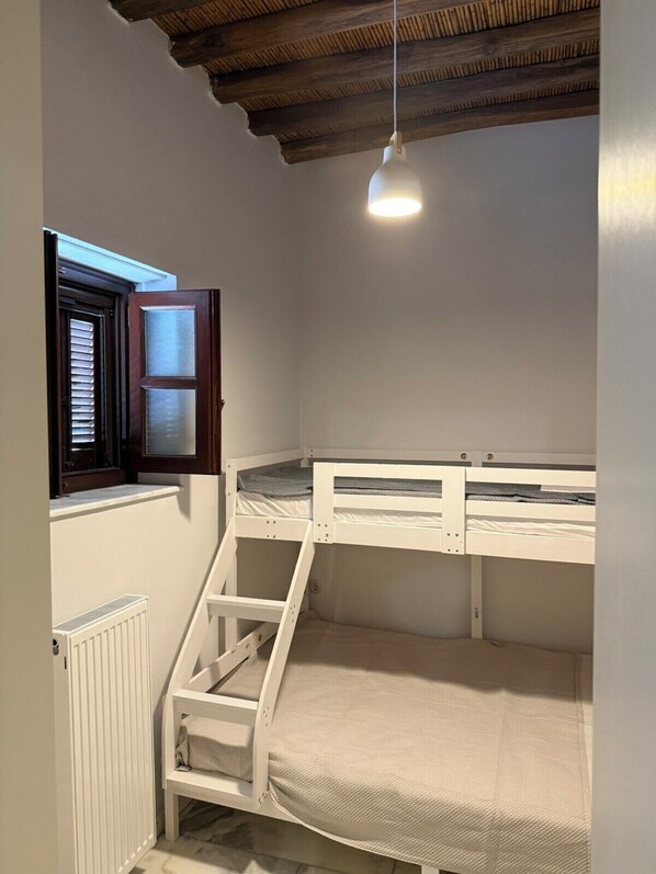 A room with a bunk bed, a window with blinds, a radiator, and a hanging light fixture.