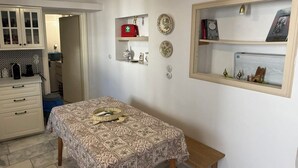 A room with a patterned table, a small wooden bench, a shelf with decorative items, and a framed picture on the wall.