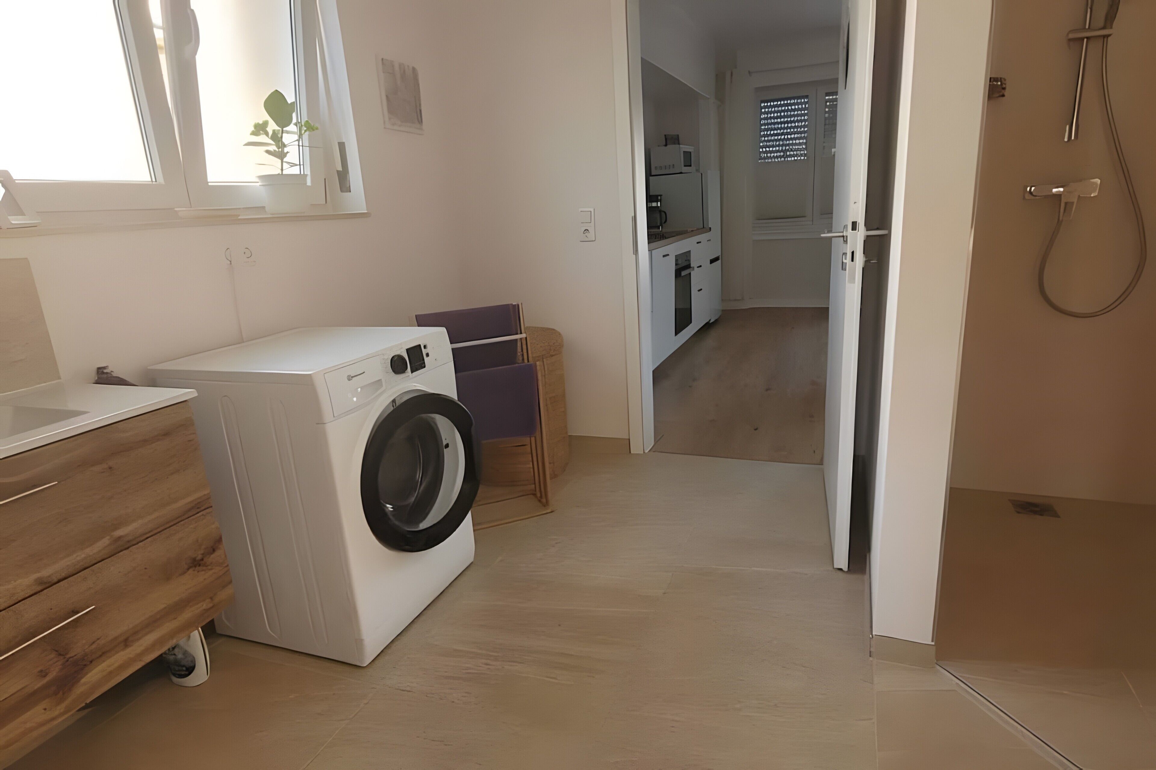 Un área de lavandería con lavadora, un gabinete de madera y una pequeña mesa con un cojín morado.