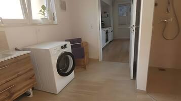 Un área de lavandería con lavadora, un gabinete de madera y una pequeña mesa con un cojín morado.