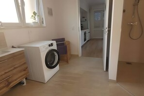 A laundry area with a washing machine, a wooden cabinet, and a small table with a purple cushion.