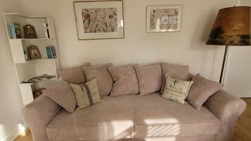 A living room with a beige sofa, striped cushions, a bookshelf, and two framed floral paintings.