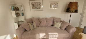 A living room with a beige sofa, striped cushions, a bookshelf, and two framed floral paintings.