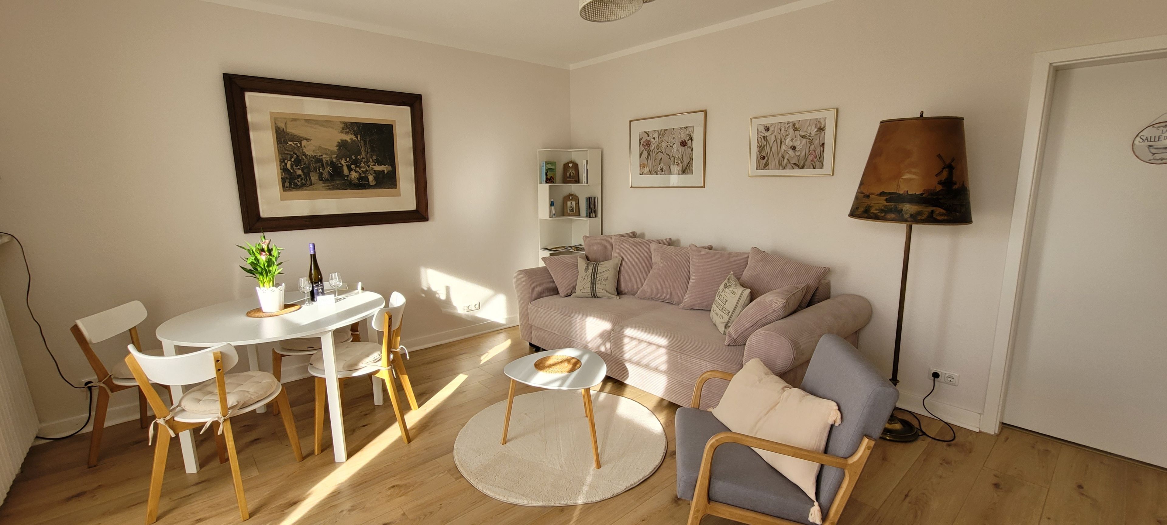 Un salon avec un canapé, une table à manger et des chaises, une lampe et des tableaux encadrés accrochés au mur.