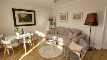 Un salon avec un canapé, une table à manger et des chaises, une lampe et des tableaux encadrés accrochés au mur.
