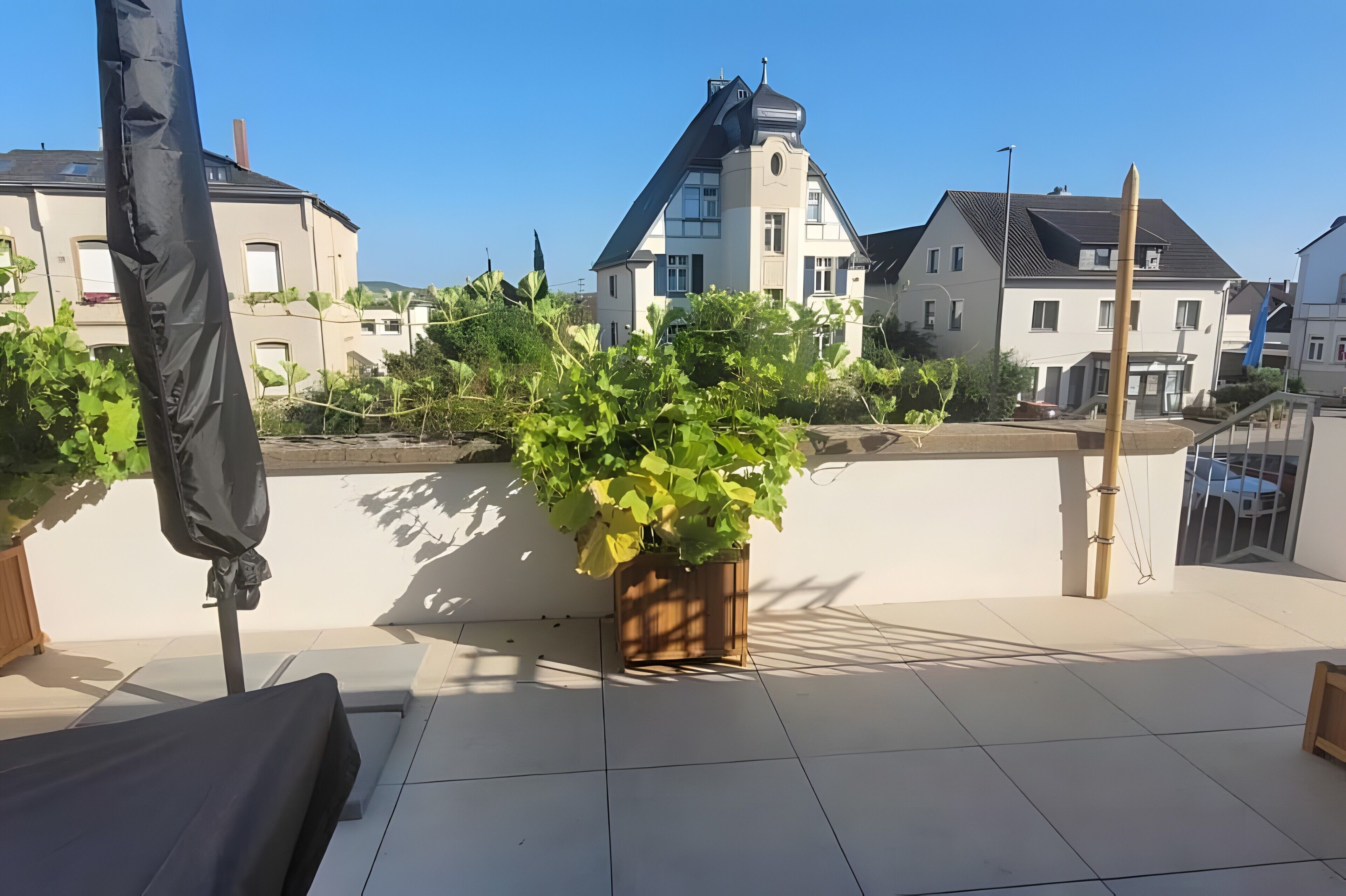 Terraza en la azotea con planta en maceta, zona de estar cubierta y vista de edificios residenciales.