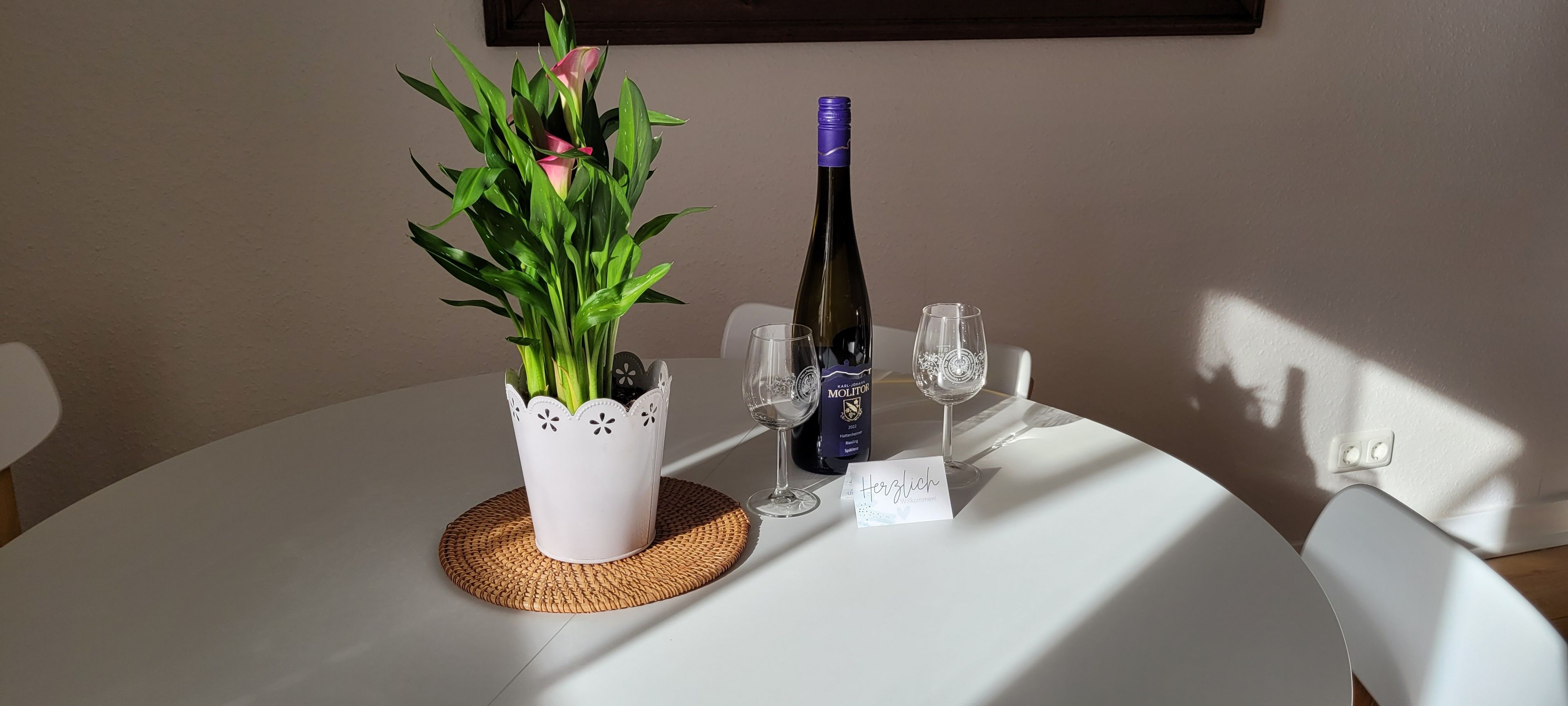 Ett runt bord med en krukväxt, en vinflaska, två glas och en servett.