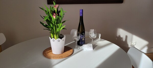 Una mesa redonda con una planta en maceta, una botella de vino, dos copas y un mantel individual.