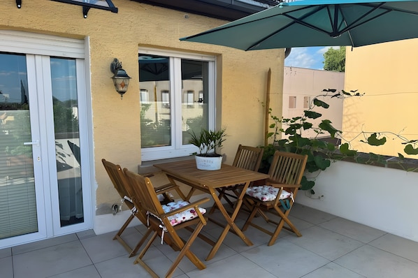 Un patio al aire libre con una mesa y sillas de madera, una planta en maceta y un paraguas grande.