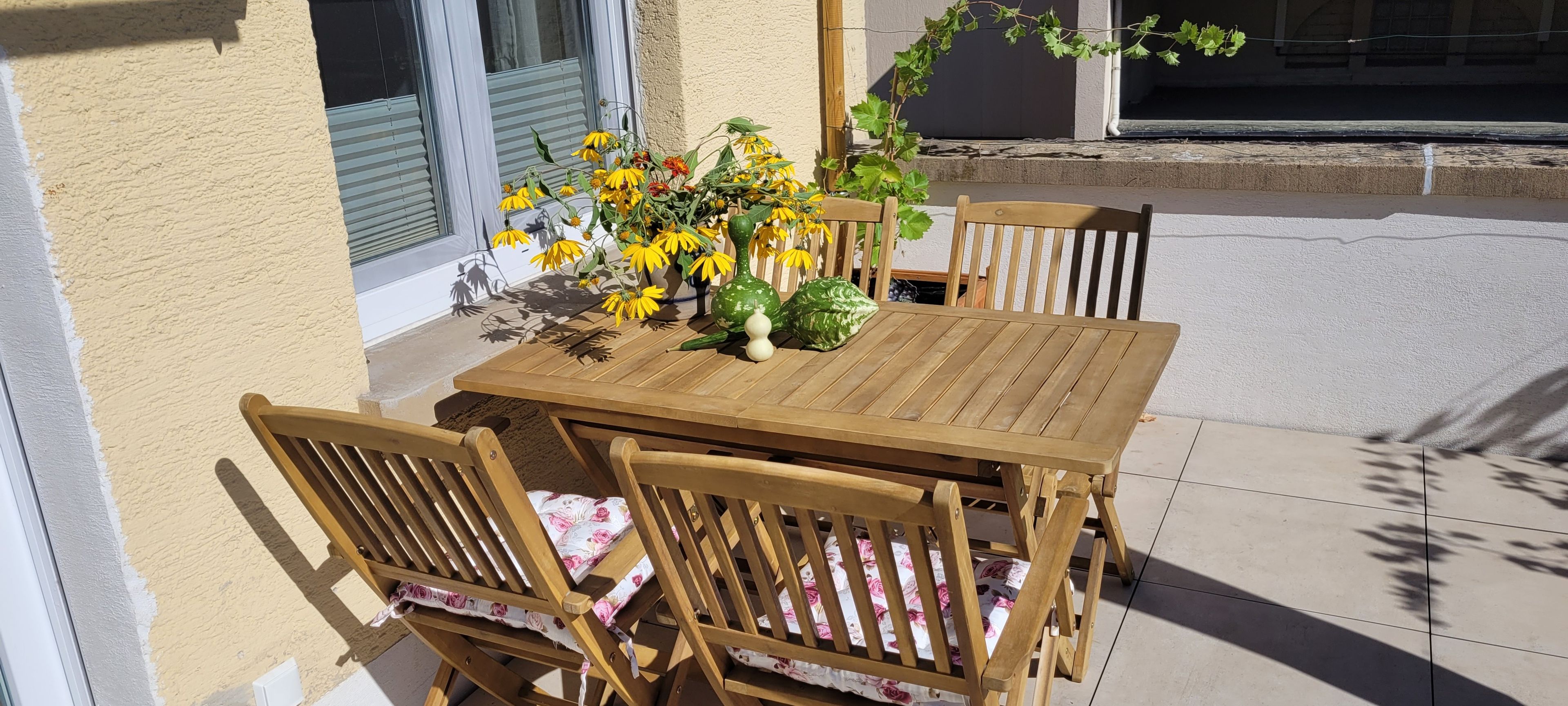 A wooden table and chairs set on a patio with a flower arrangement.