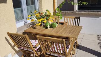 A wooden table and chairs set on a patio with a flower arrangement.