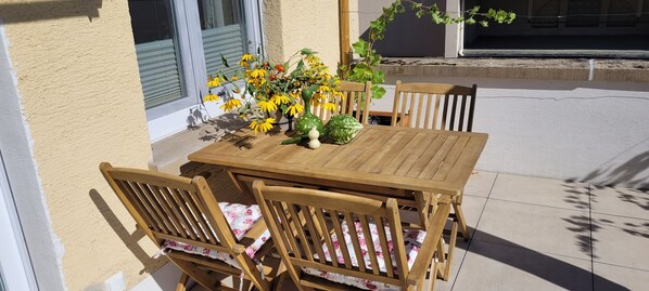 Ett träbord och stolar står på en uteplats, och en blomsteruppsättning pryder bordet.