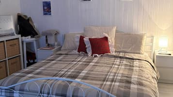 Una camera da letto con una struttura letto in metallo, una coperta a quadri e due cuscini. Sono presenti due comodini con lampade, una sedia e una scrivania con un computer.