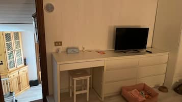Una stanza con una scrivania bianca, una televisione, uno sgabello e un lettino rosa per animali domestici.