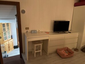 A room with a white desk, a television, a small stool, and a pink pet bed. - A charming, renovated, and furnished two-story apartment in the historic center (Tagliacozzo)