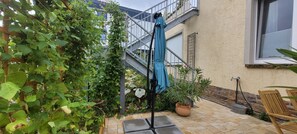 A patio with a metal umbrella stand, potted plants, and a wooden chair. - Pet-friendly apartment 'Linus' (Geisenheim)