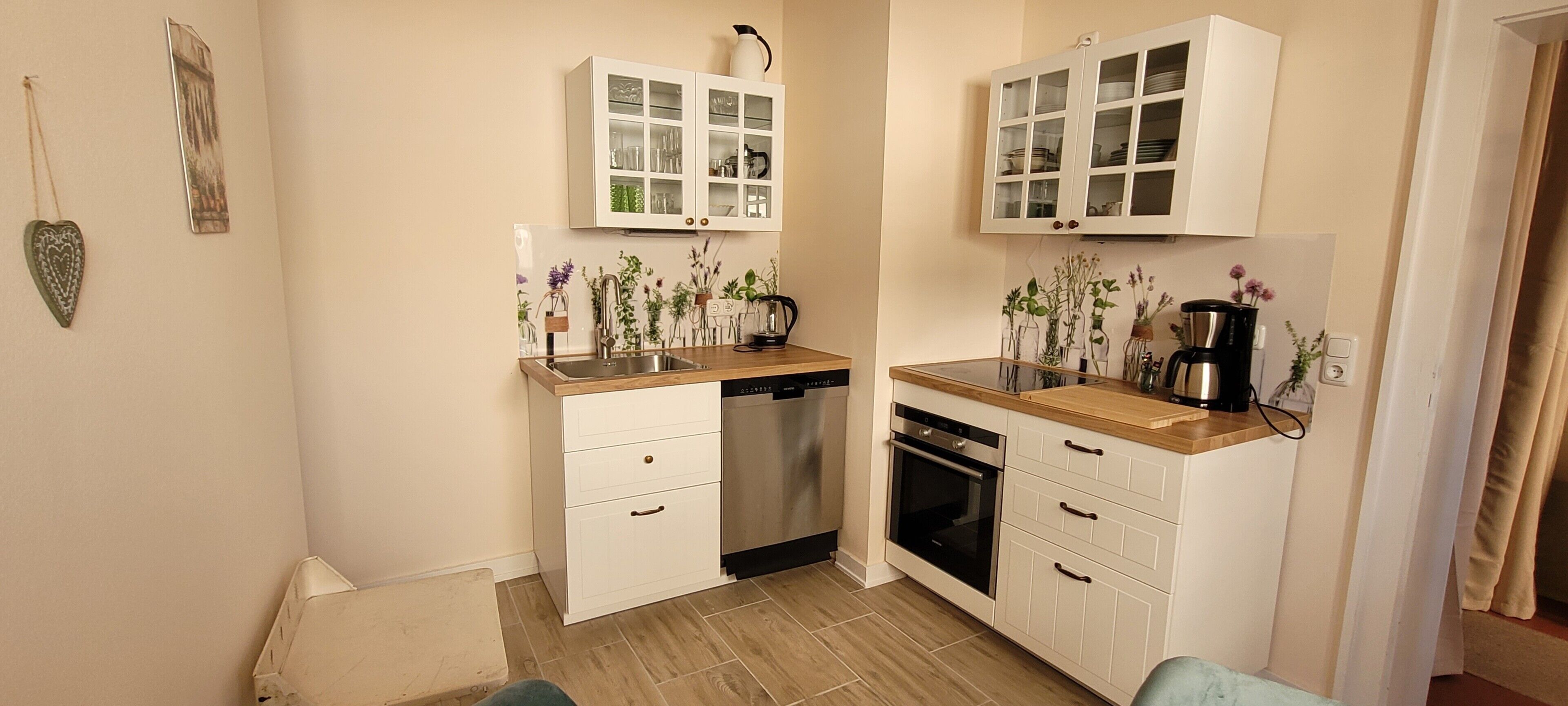 A compact kitchen with white cabinetry, a dishwasher, an oven, and a coffee maker.