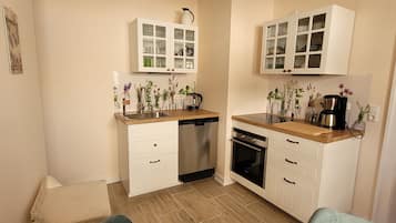 A compact kitchen with white cabinetry, a dishwasher, an oven, and a coffee maker.