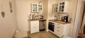 A compact kitchen with white cabinetry, a dishwasher, an oven, and a coffee maker.