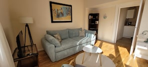 A living room with a sofa, a small table, a lamp, and a framed artwork on the wall.