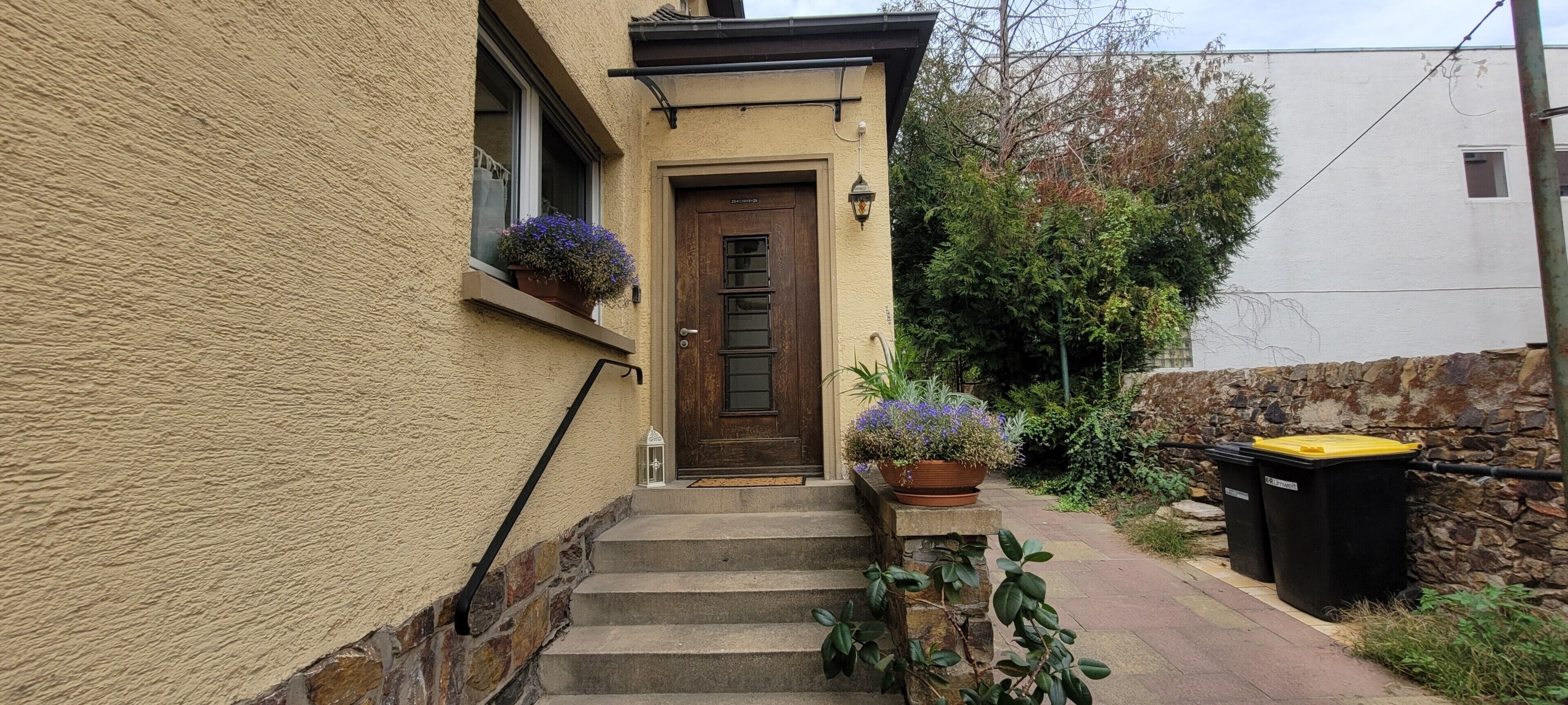 Een huis met een houten deur, een paar treden die naar de ingang leiden en een stenen muur.