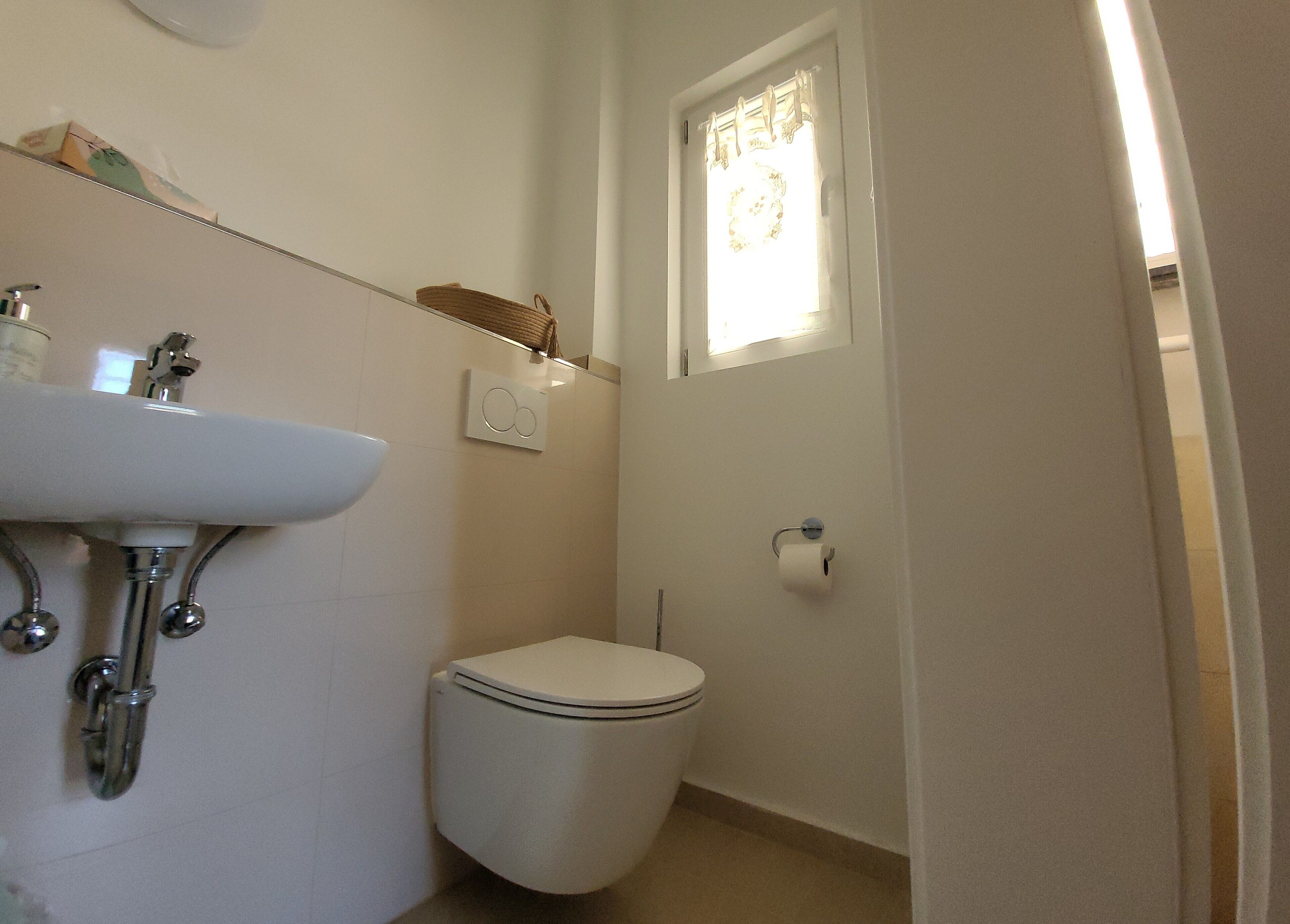 Ein Badezimmer mit Waschbecken, Toilette und einem Fenster mit Vorhang.