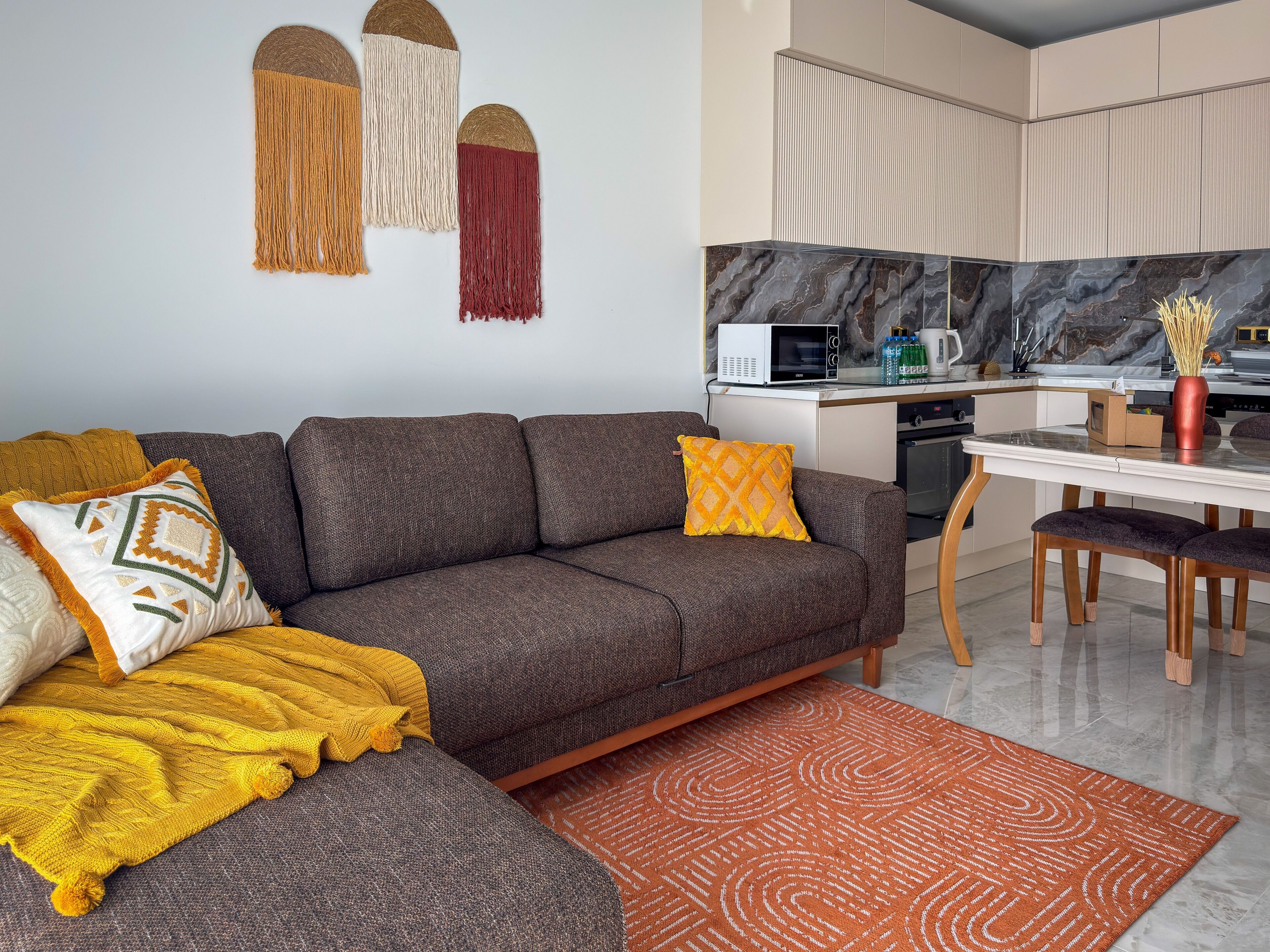 Ein modernes Wohnzimmer mit einer Couch, einer gemusterten Decke und einer Küchenzeile mit Mikrowelle und Schränken.