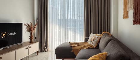 Una sala de estar moderna con un sofá, un televisor y una ventana con cortinas.