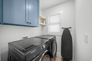 A laundry room with a Samsung washer and dryer, a window with blinds, and a blue cabinet. - Brand New - Gorgeous 3 Bedroom 3 Bathroom (Naples)