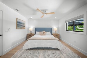 A bedroom with a bed, bedside lamps, a ceiling fan, a window with a view, and a painting on the wall. - Brand New - Gorgeous 3 Bedroom 3 Bathroom (Naples)