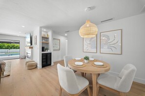 A modern dining area with a round wooden table, white chairs, and a hanging light fixture. - Brand New - Gorgeous 3 Bedroom 3 Bathroom (Naples)