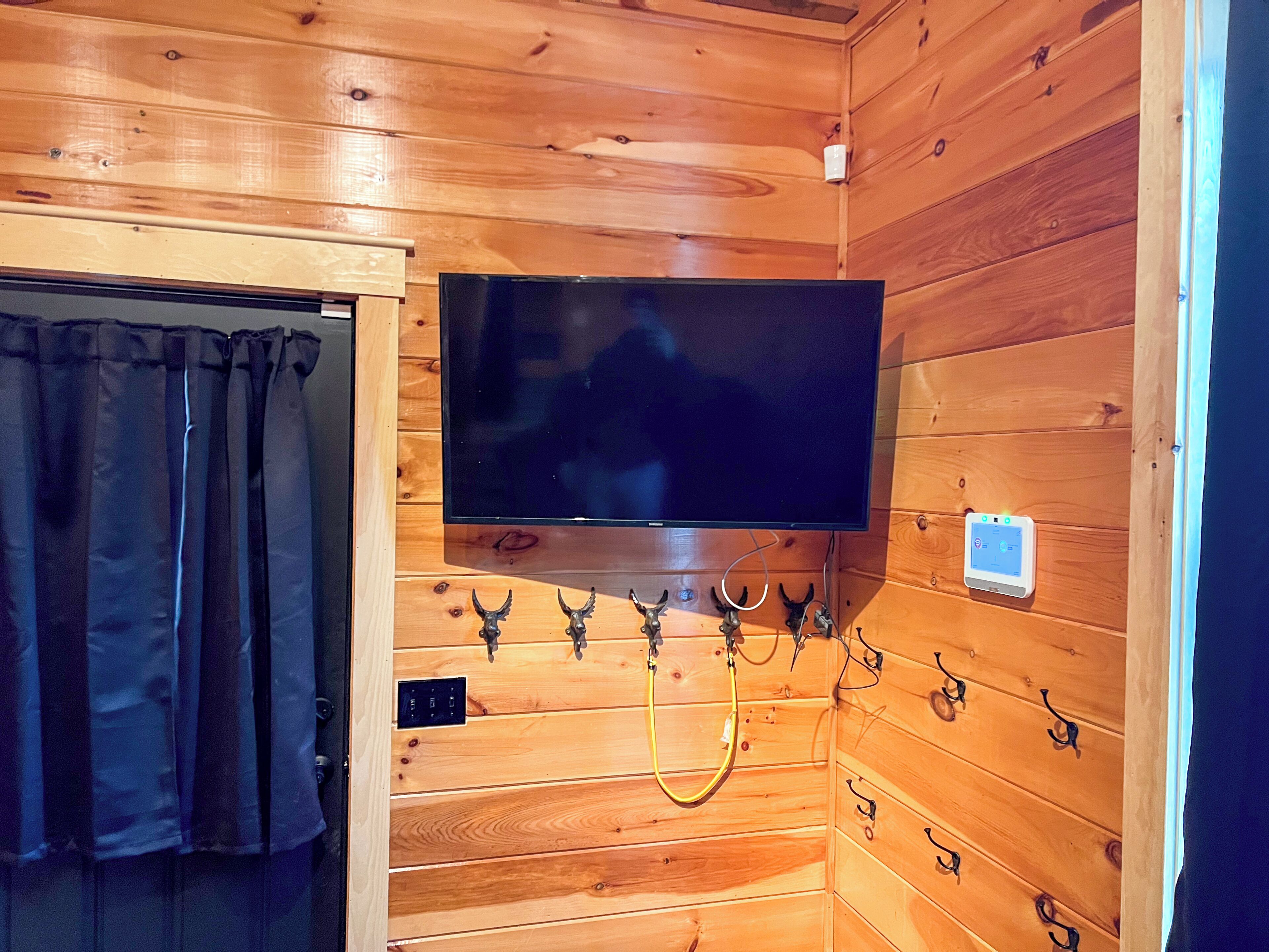 A wooden-paneled room with a mounted television, a curtain, and a wall-mounted thermostat.