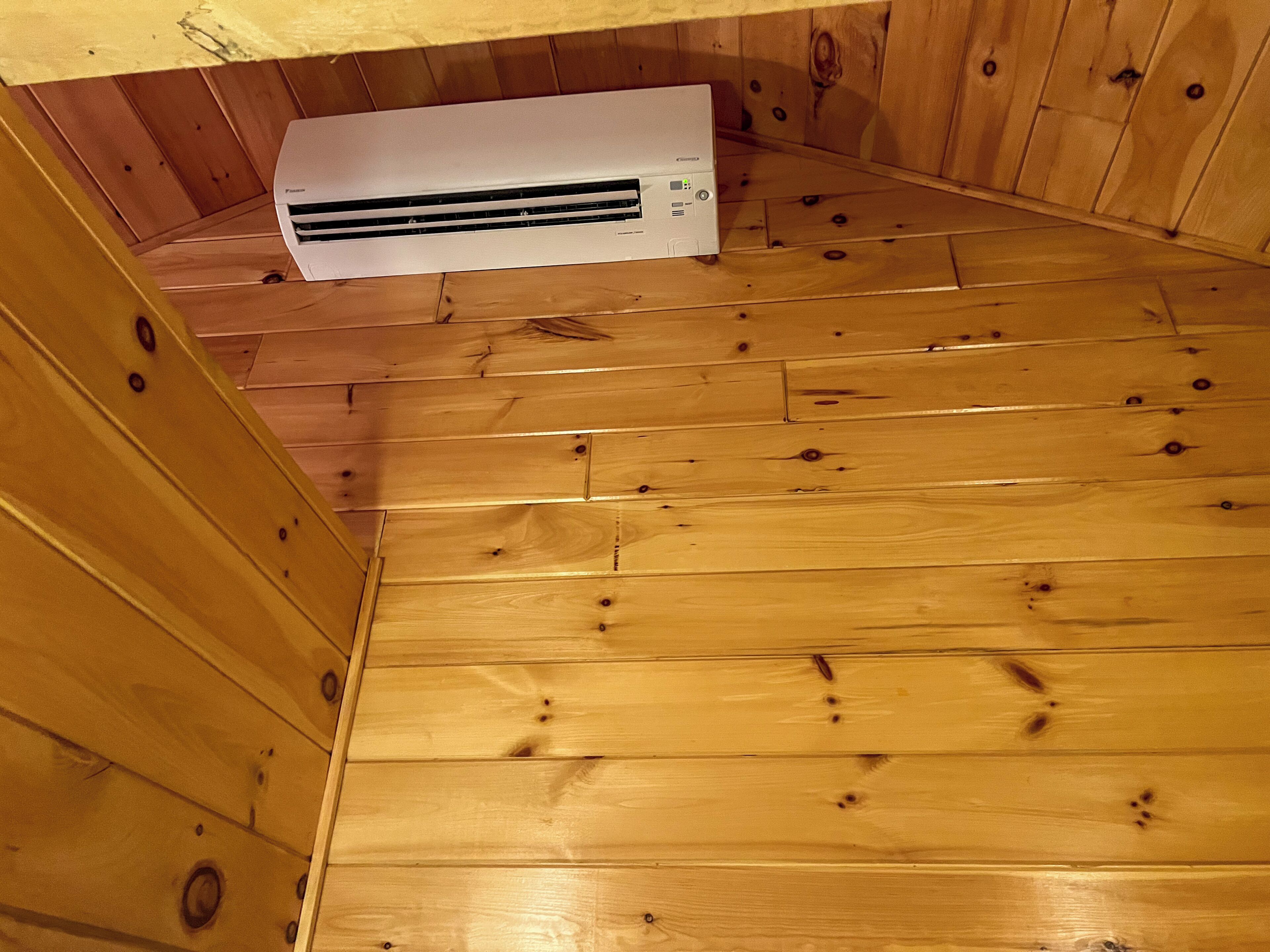 Ein Zimmer mit Holzboden und einer weißen Wandairconditioner.