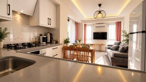 A modern kitchen with a central island, dining area with wooden furniture, and a living room with a sofa and TV. - Olivara Süite (Muğla)