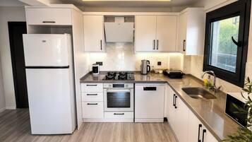 Una cocina moderna con armarios blancos, horno empotrado, refrigerador y una ventana con persianas.