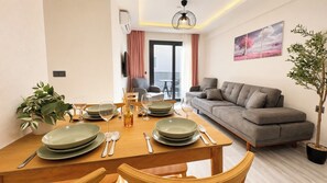 A dining area with a wooden table set for four, a grey sofa, and a potted plant. - Olivara Süite (Muğla)