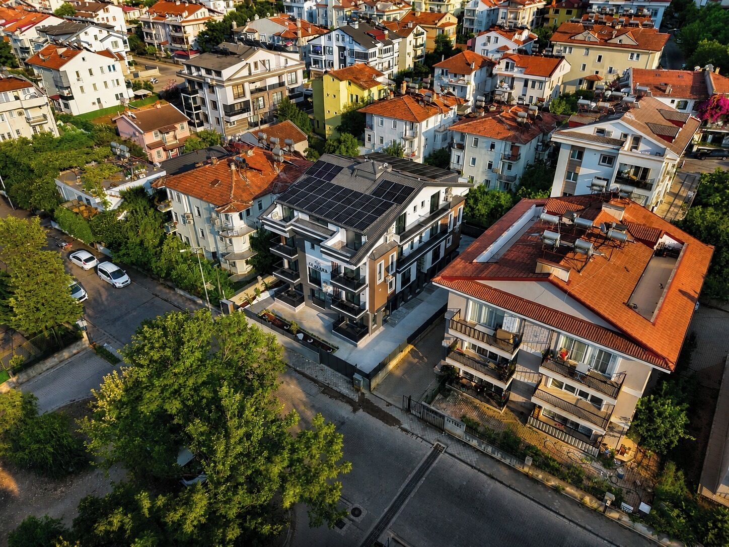 A residential area with multi-story buildings, some with solar panels, and a street with parked cars.