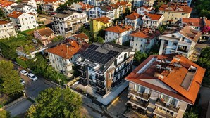 Un barrio residencial con edificios de varios pisos, algunos con paneles solares, y una calle con coches estacionados.