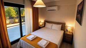 Habitación de hotel con cama, dos mesitas de noche, ventana con cortinas, aire acondicionado y un cuadro en la pared.