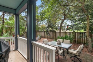 Ein überdachter Patio-Bereich mit Tisch und Stühlen, umgeben von einem Holzzaun und Bäumen.
