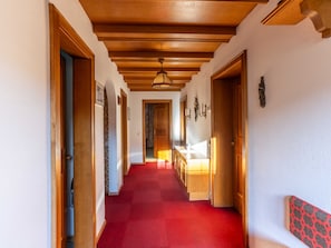A hallway with wooden doors, a red carpet, and a chandelier.
