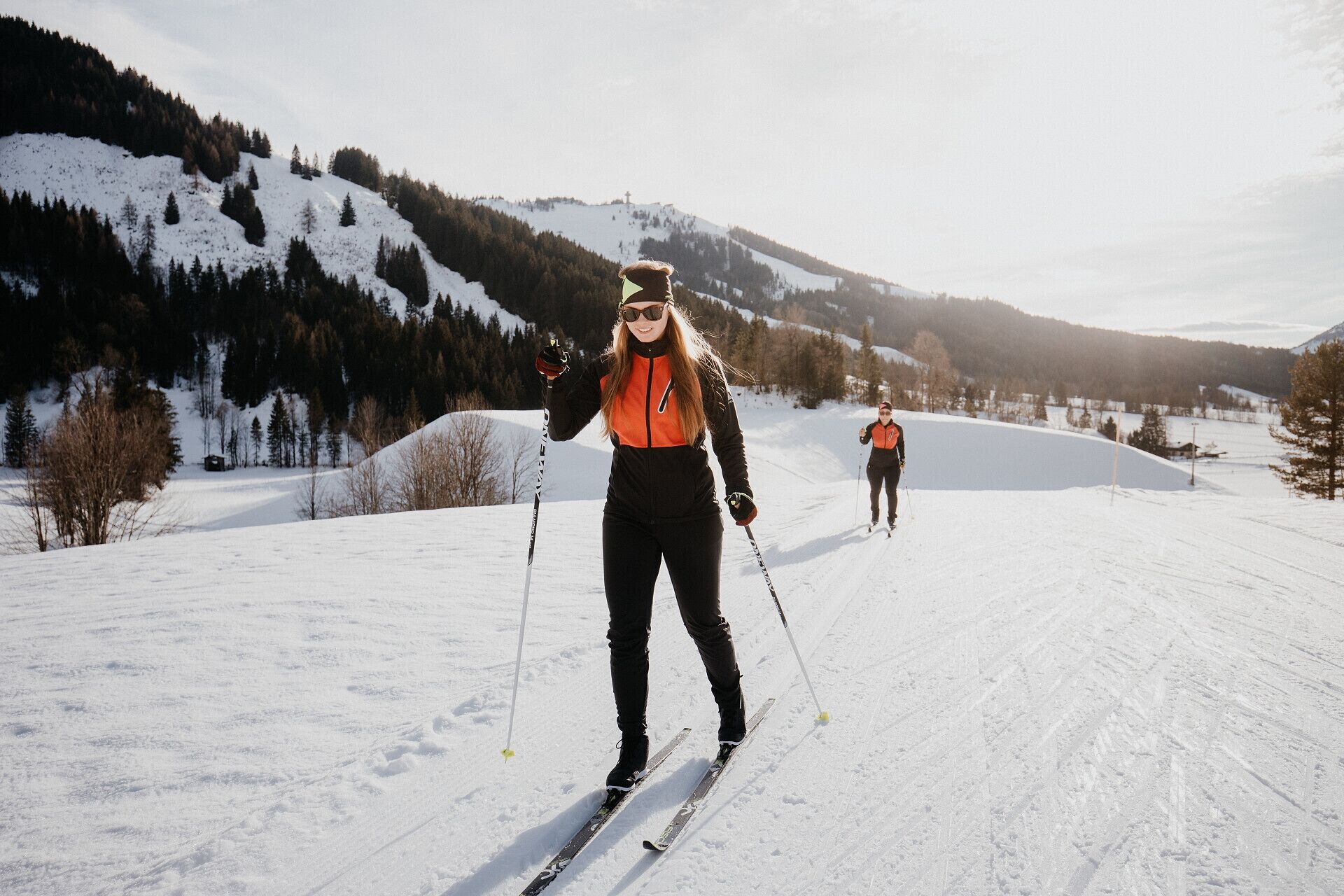 A person skiing on a snow-covered path with trees and hills in the background.