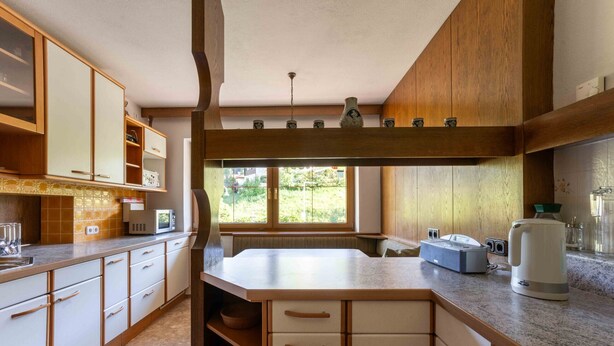 Una cucina con mobili in legno, un piano di lavoro, un forno integrato e una finestra che lascia entrare luce naturale.