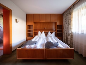 A bedroom with a wooden bed frame, a built-in wardrobe, and a window with curtains.