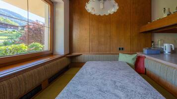 Eine Küche mit Holzausstattung, einer Marmorarbeitsplatte, einer integrierten Bank, einer Pendelleuchte und Blick auf einen Garten durch ein großes Fenster.