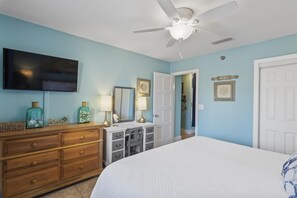 A bedroom with a bed, dresser, vanity, and a ceiling fan. - Seafarer 108- The Peachy Pelican (Destin)