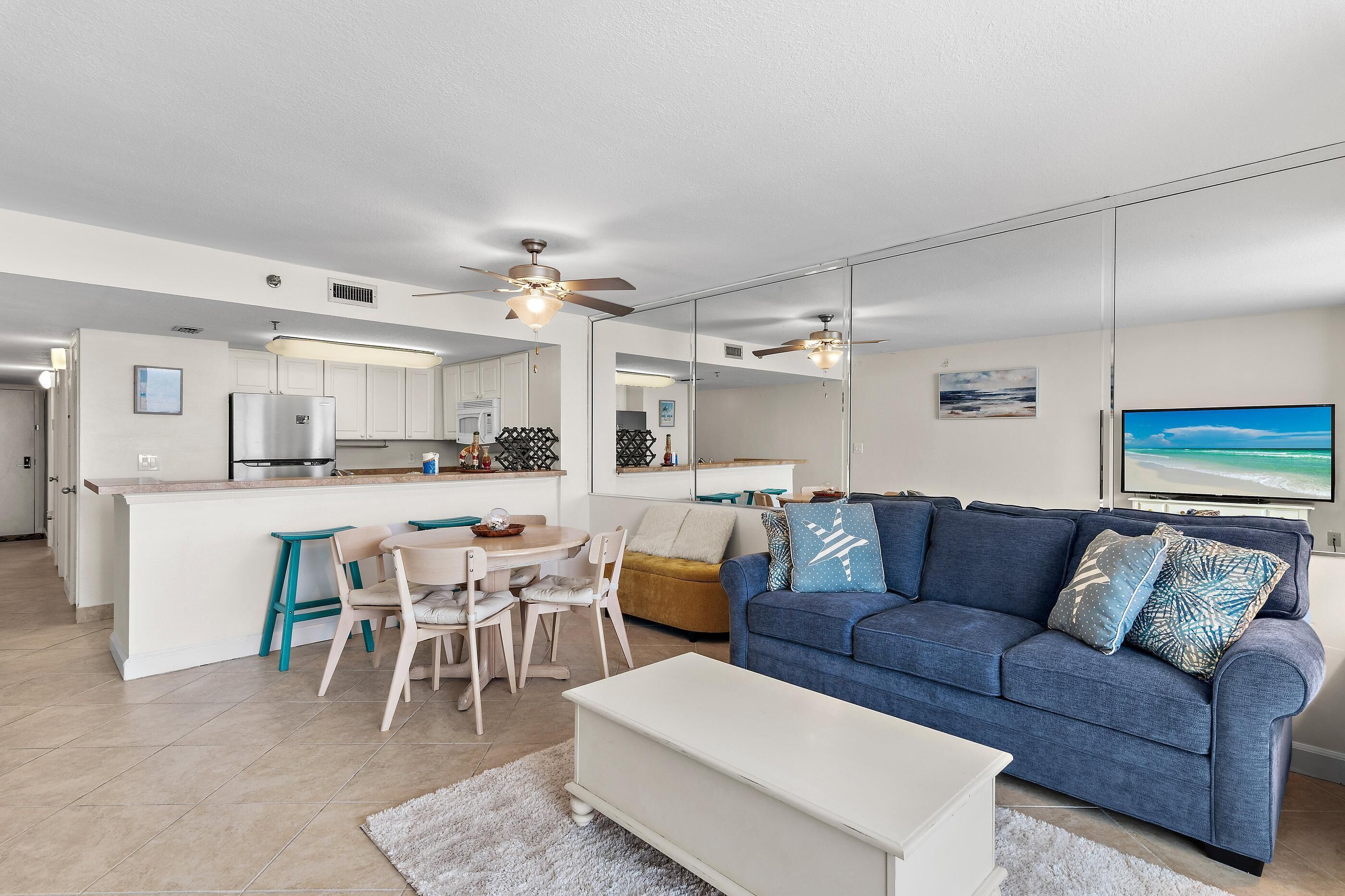 A modern living room with a blue sofa, a white coffee table, and a dining area with a wooden table and chairs.