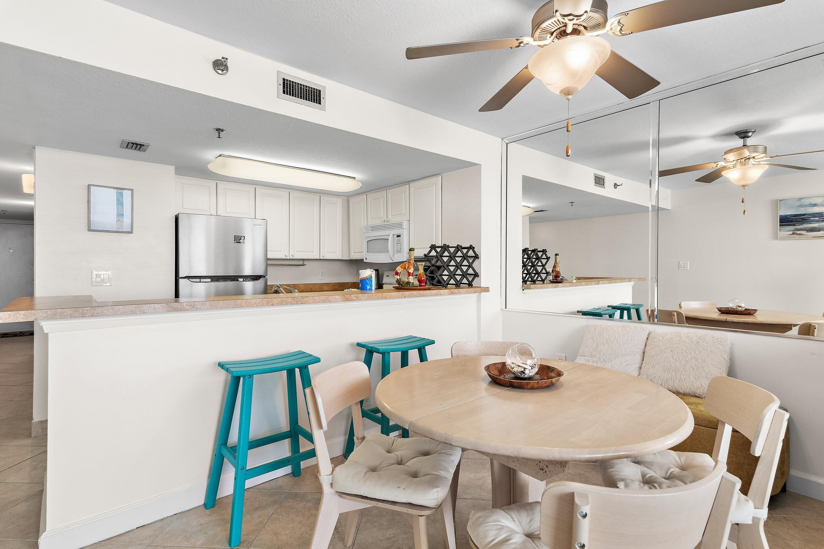 A modern kitchen with white cabinets, a stainless steel refrigerator, a microwave, and a ceiling fan.
